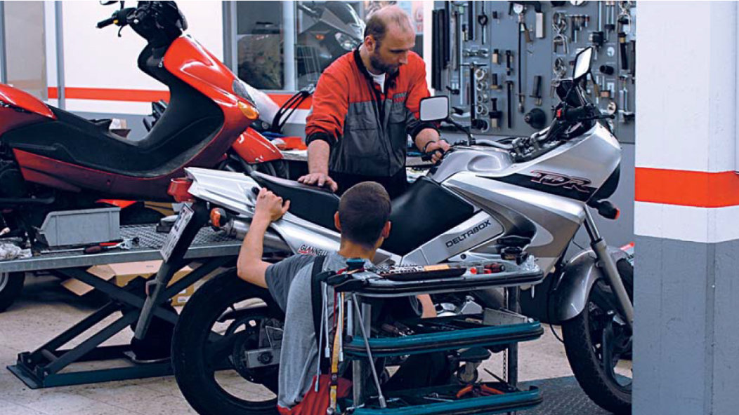 Foto di un'officina in cui due persone stanno lavorando su una moto.