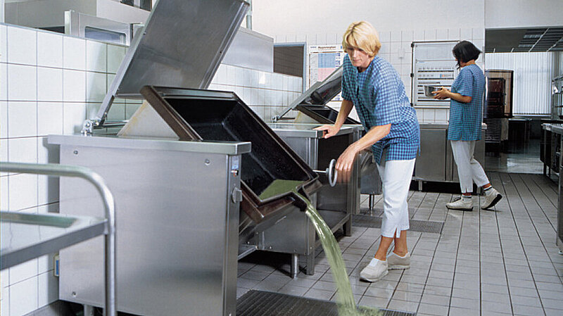 In una cucina industriale, un grande recipiente di cottura viene svuotato in una Vasca a pavimento. In una cucina industriale, un grande recipiente di cottura viene svuotato in una Vasca a pavimento.